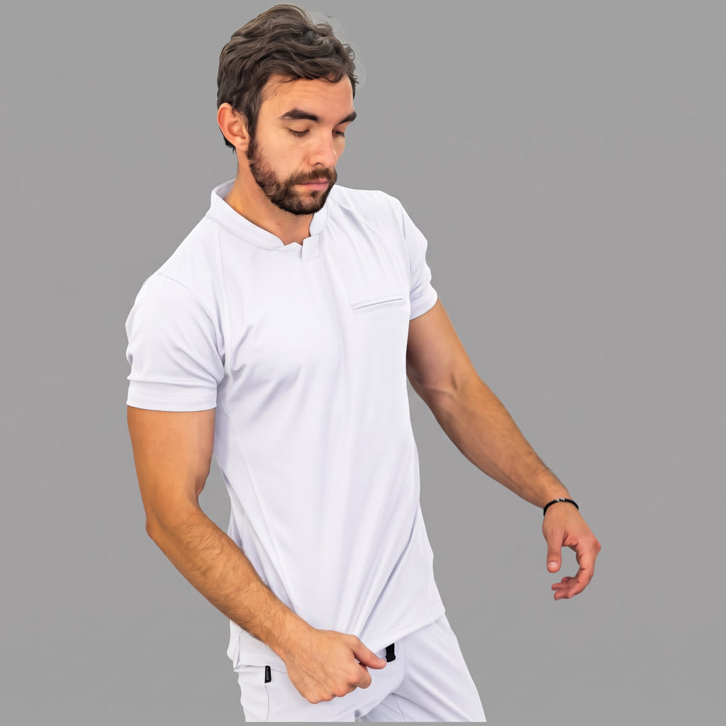 scrubs-blanco-mirada-abajo.jpg: "Modelo mirando hacia abajo con la filipina quirúrgica Est. 910 blanca, mostrando su corte slim fit y el bolsillo del pecho con cierre."